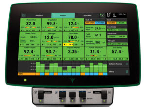 Das 20|20® Terminal von Precision Planting zeigt eine detaillierte Benutzeroberfläche mit grünen Informationsfeldern für Saatpopulation, Singulation, Stickstoffverteilung, Bodenfeuchtigkeit, Temperatur und weitere Messwerte während der Aussaat. Darunter befindet sich eine Bedienkonsole mit mehreren Schaltern zur Steuerung von Last, Abschnittskontrolle und Master-Funktion.