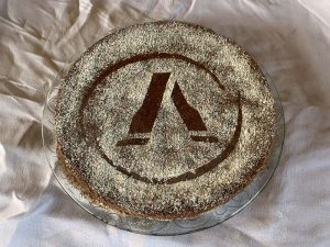 Runder Kuchen auf einer Glasplatte, dekoriert mit Puderzucker, der das Agrisem-Logo als Muster zeigt. Der Kuchen liegt auf einer weißen Tischdecke. Foto aufgenommen am 13.06.2025.