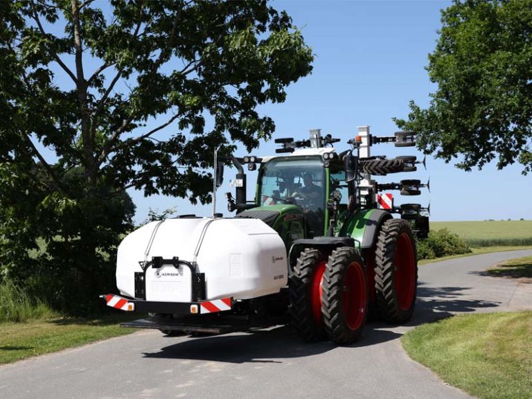 Ein grüner Traktor mit roter Bereifung fährt auf einer Landstraße. Vorne ist ein weißer Fronttank DSL von AGRISEM montiert. Am Heck des Traktors ist die AGRISEM SCALP Maschine zu sehen. Im Hintergrund stehen Bäume und Felder unter blauem Himmel.