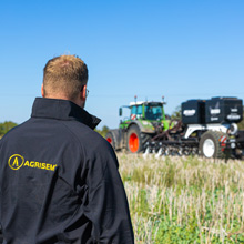 Ein Mann mit Agrisem-Jacke blickt auf die Agrisem BOSS, die von einem Traktor auf einem Feld gezogen wird.