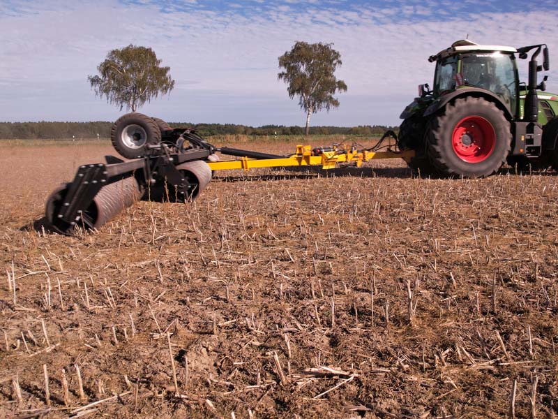 Agrisem Pack Roller mit ausgeklapptem Walzensegment hinter einem Traktor bei der Bodenbearbeitung auf einem abgeernteten Feld.
